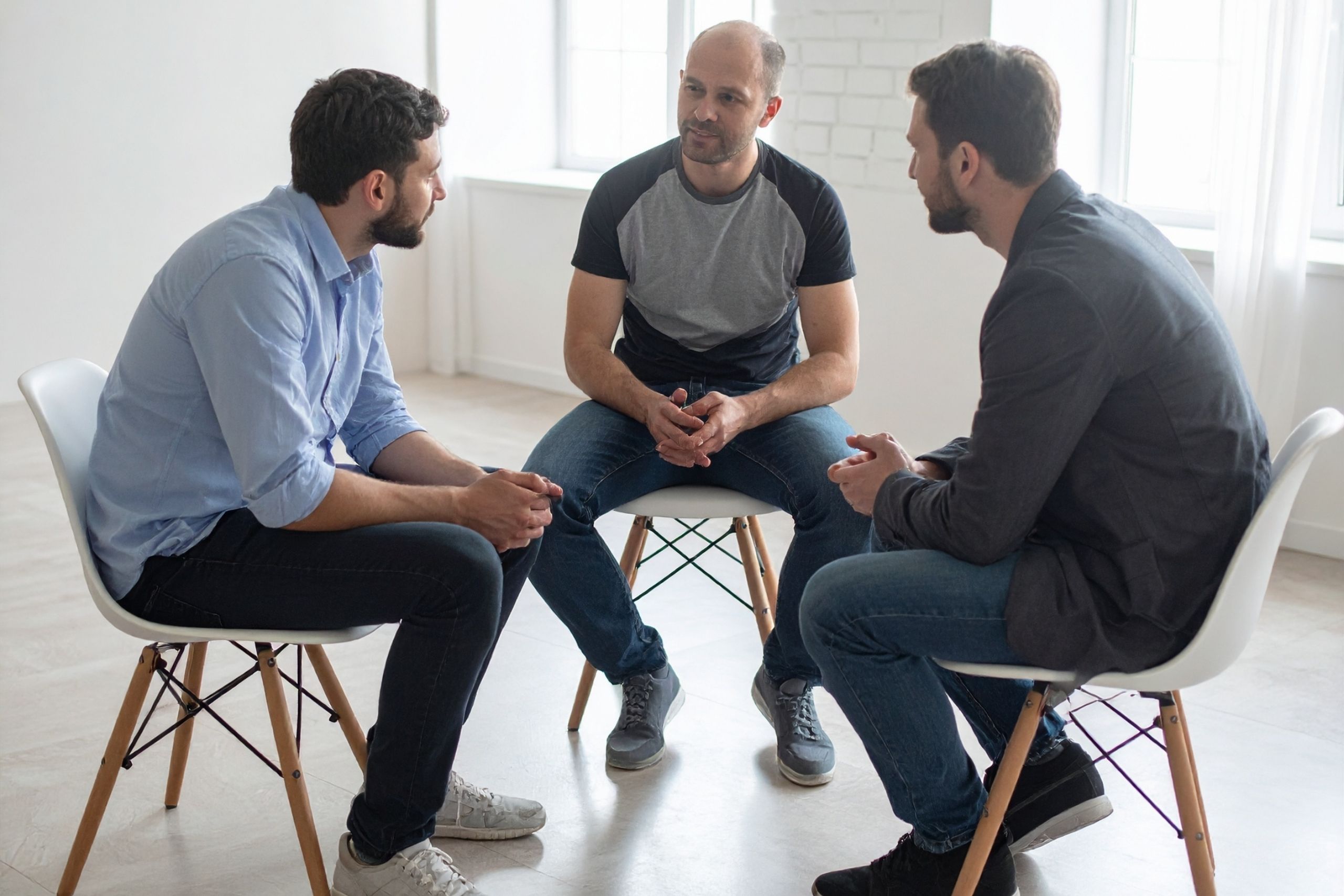 Drei Männer sitzen auf Stühlen im Kreis