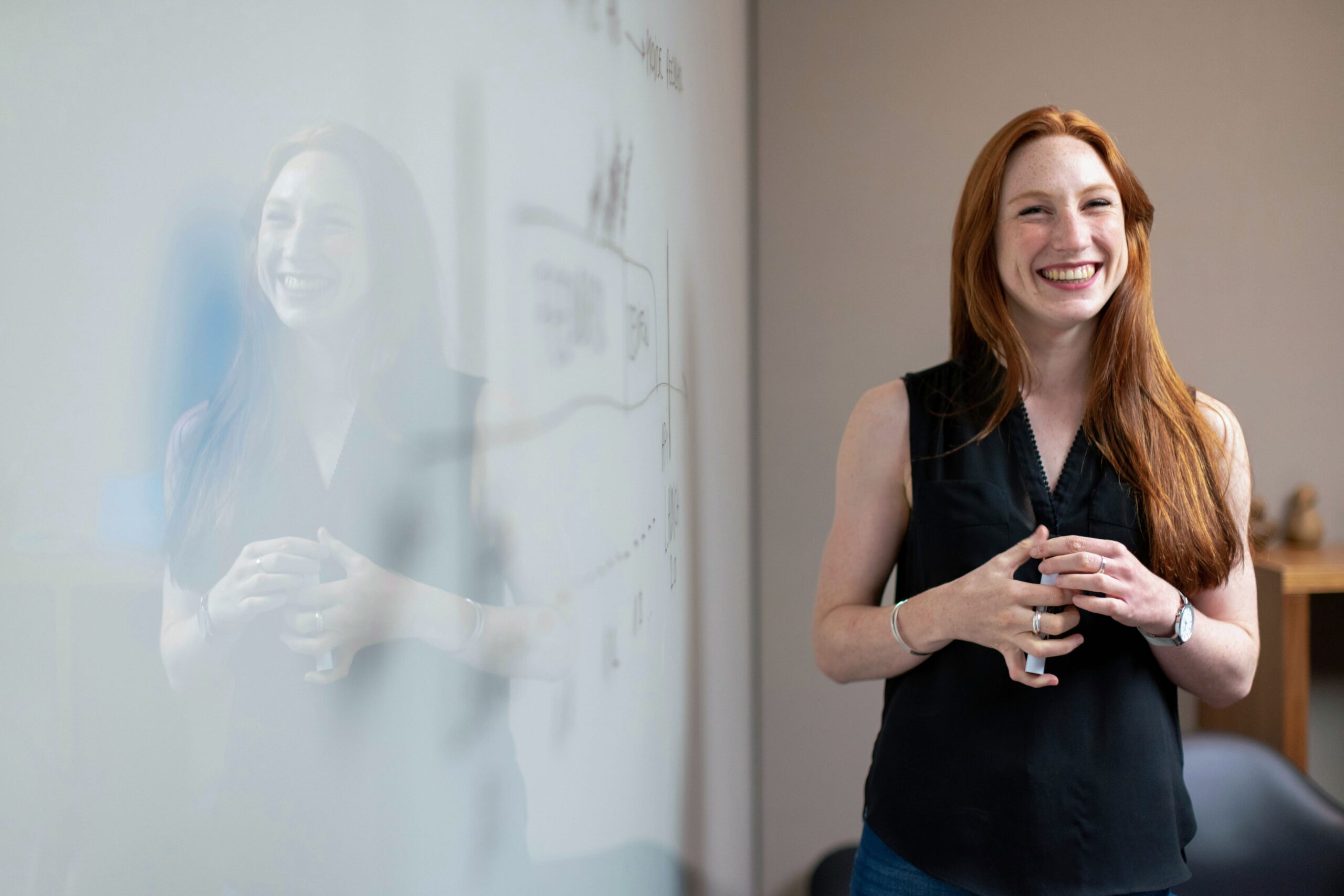 Rothaarige Frau steht lächelnd vor Whiteboard